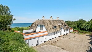 Een traditioneel rieten huis met een witte gevel, een grindpad en uitzicht op zee.
