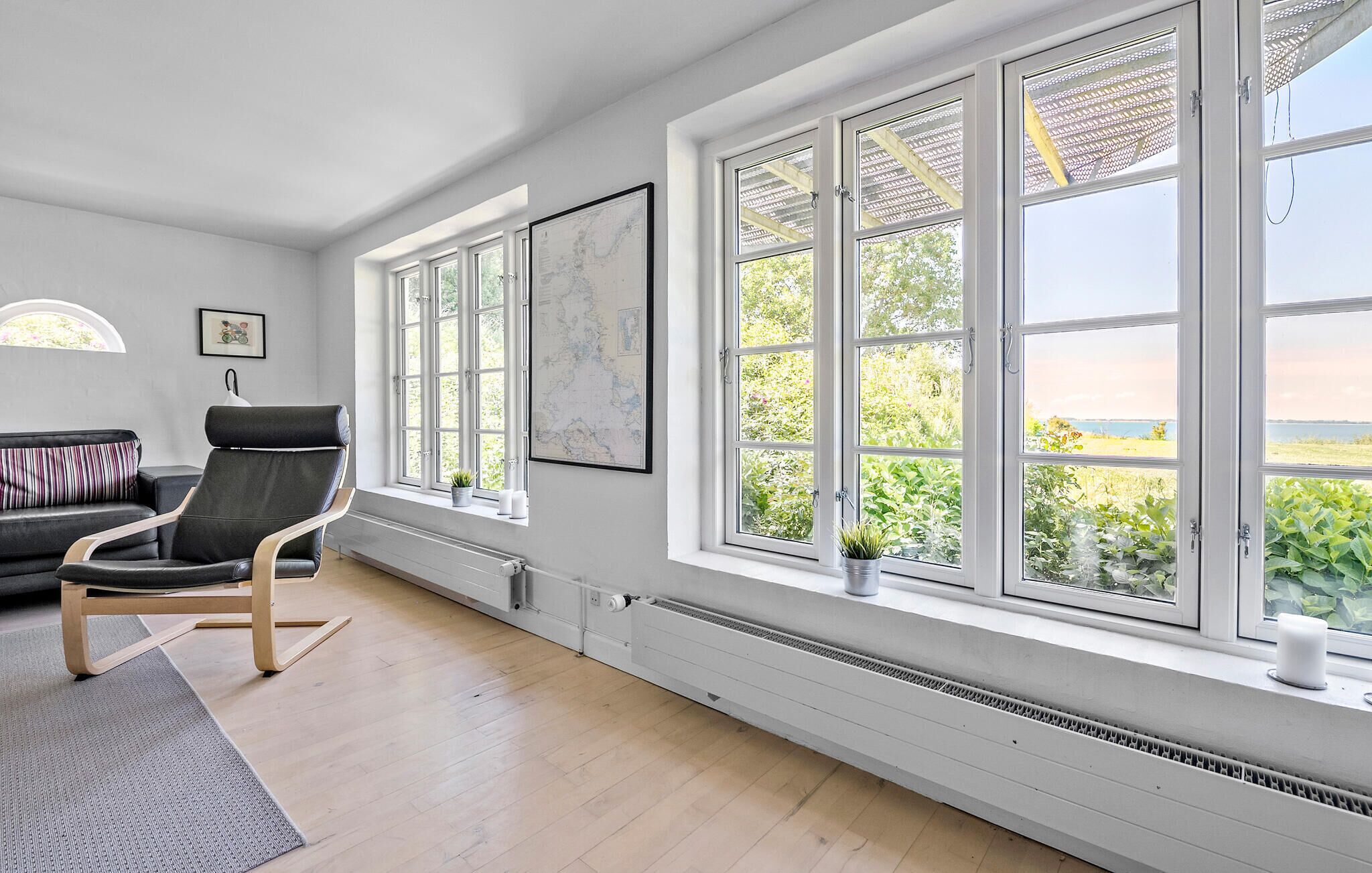A spacious room with large windows, a black leather chair, a white radiator, and a framed map on the wall.