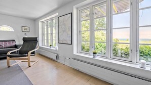 Een ruime kamer met grote ramen, een zwarte leren fauteuil, een witte radiator en een lijst met een kaart aan de muur.