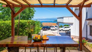 Une terrasse extérieure avec une table dressée pour deux personnes, un vase rempli de fleurs et un saladier de fruits.