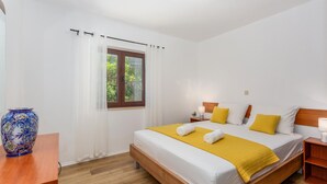 Une chambre à coucher avec un lit, une fenêtre avec des rideaux, une table de chevet avec une lampe et un vase décoratif.