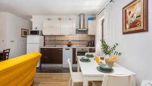 Une cuisine compacte avec des meubles blancs, une hotte en acier inoxydable et un coin repas comprenant une table et des chaises blanches.
