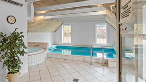 Et moderne poolområde indendørs med jacuzzi, flisegulv, træbjælker i loftet og store vinduer, der lukker naturligt lys ind.