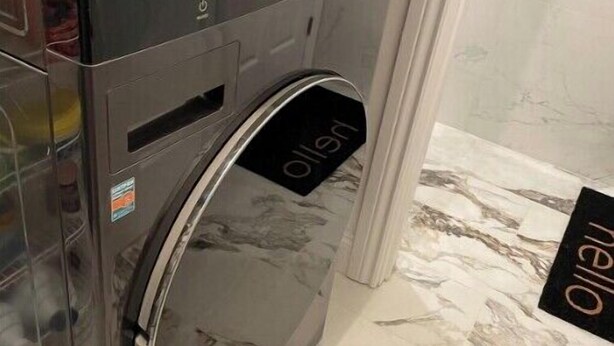 A modern, compact washer and dryer unit with a stainless steel finish, located in a room with marble flooring.
