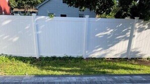 A paved patio area with a white fence and a house in the background.