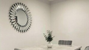 A dining area with a rectangular table, four grey upholstered chairs, a potted plant, and a circular wall decoration.