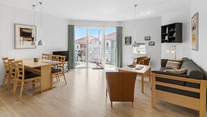 A modern living room with a dining area, a sofa, and a TV. There is a balcony with a view of buildings. - Gudhjem Søpark Lejl. 30 (Gudhjem)