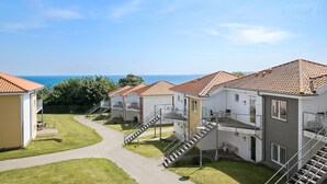 A row of two-story buildings with red-tiled roofs, a central pathway, and a view of the sea. - Gudhjem Søpark Lejl. 30 (Gudhjem)