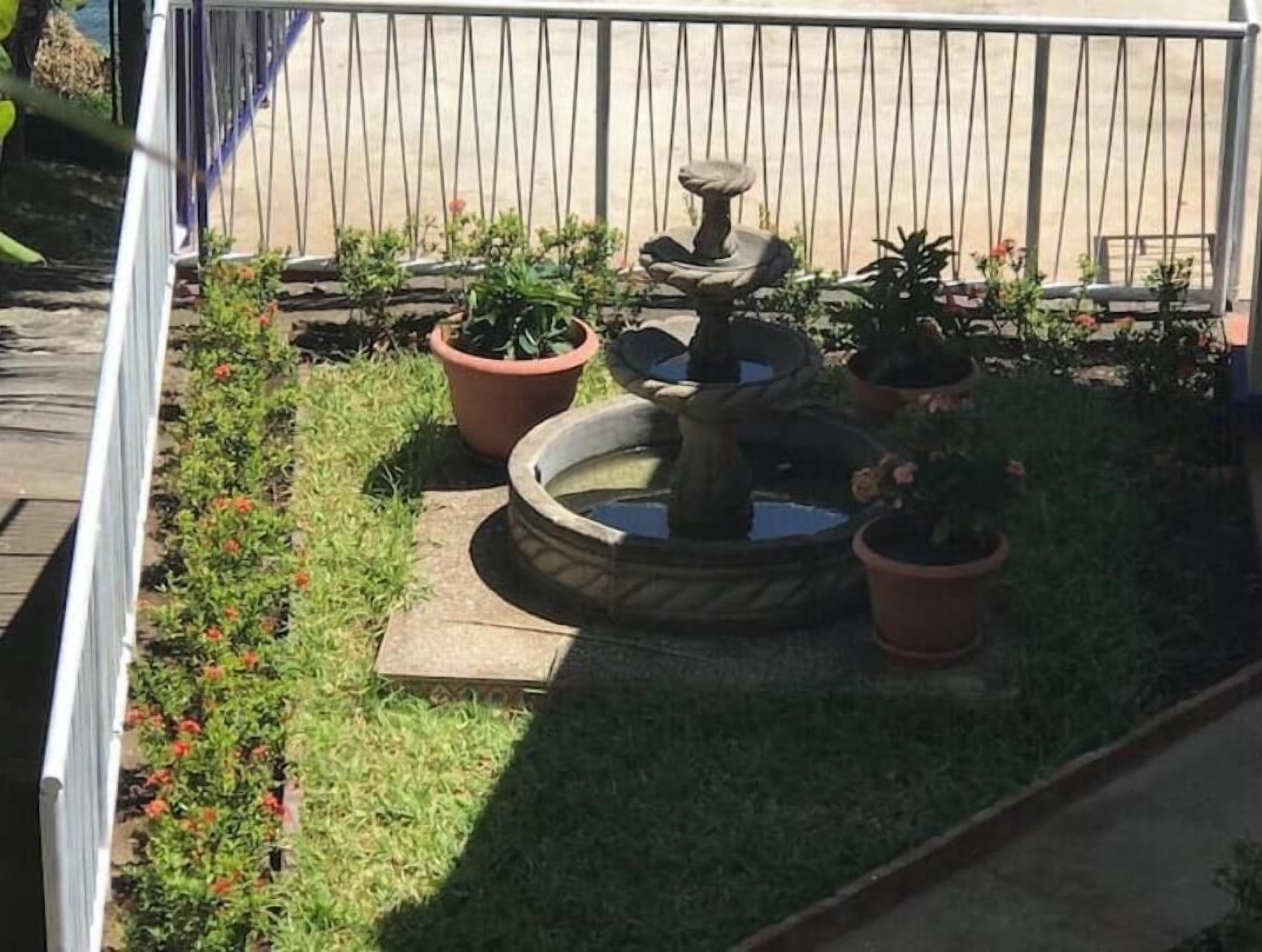 A garden with a stone fountain, potted plants, and a wooden deck.