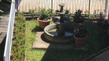 A garden with a stone fountain, potted plants, and a wooden deck.