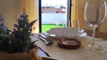 Spisebord med et glas vin, en skål og bestik. Et vindue viser udsigt til bygninger og et grønt område.