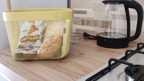 Una cocina con una cesta amarilla que contiene alimentos envasados, un hervidor eléctrico negro y una estufa.