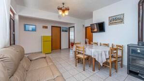 A living room with a beige sofa, a dining table with chairs, a yellow refrigerator, a TV, and a wood-burning stove. - Gorgeous home in Dobropoljana (Dobropoljana)