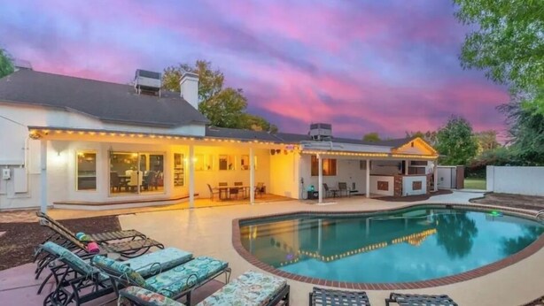 A backyard with a swimming pool, outdoor furniture, and a covered patio area.