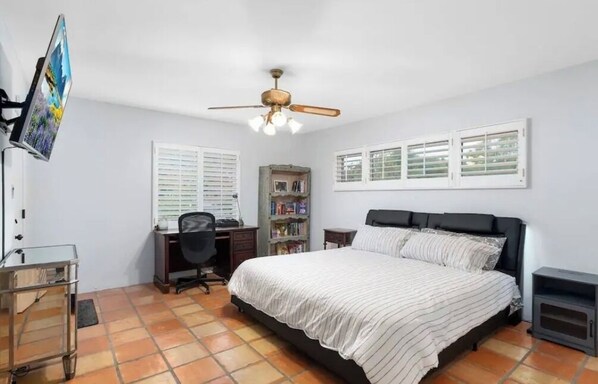 A bedroom with a bed, a desk, a chair, a bookshelf, and a TV.