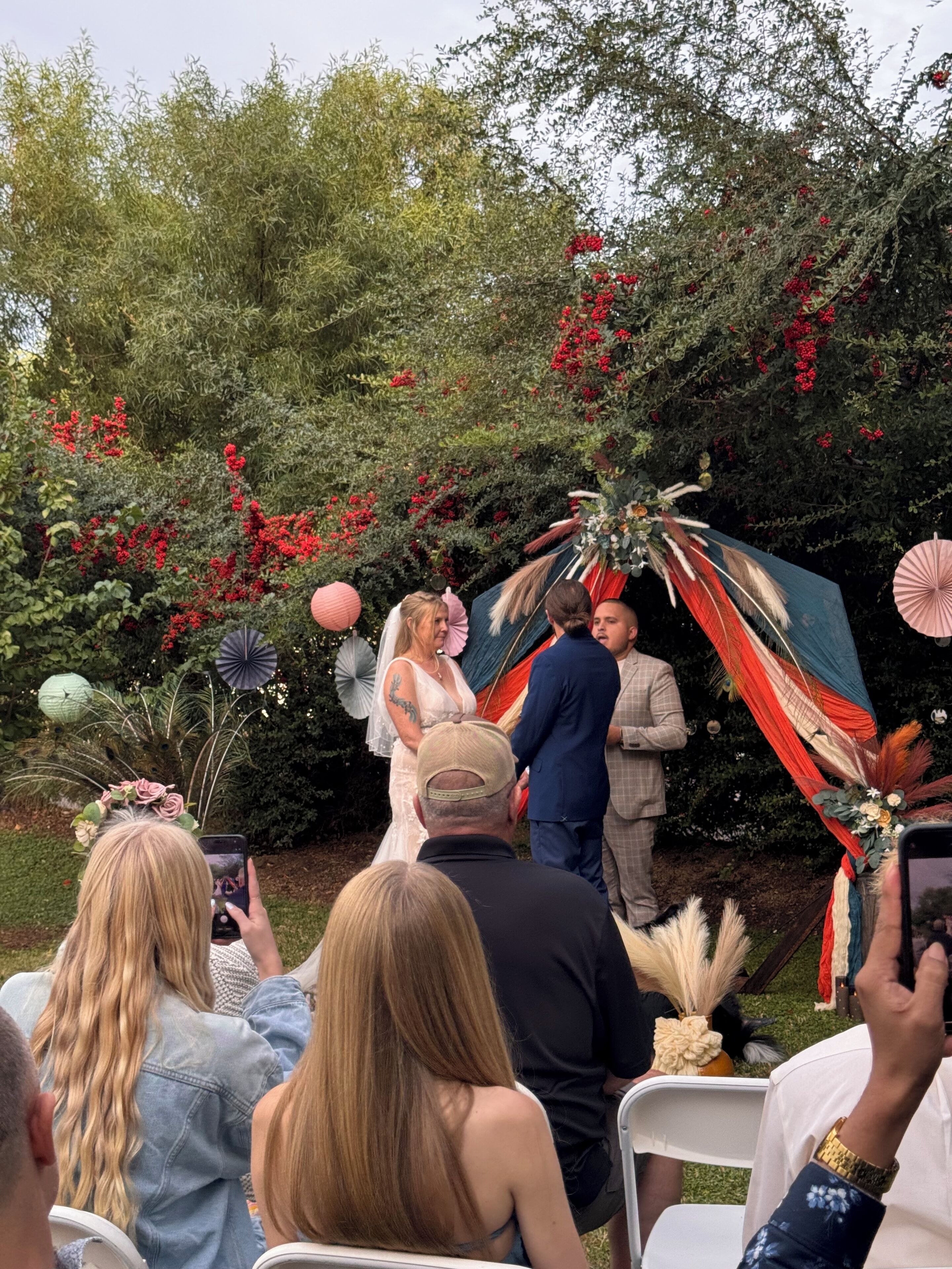 A wedding ceremony outdoors with guests seated on white chairs.
