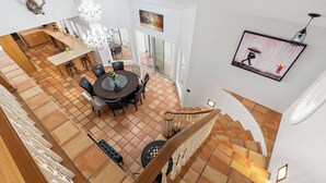 A spacious dining area with a round table and chairs, a chandelier, and a staircase leading to an upper floor.