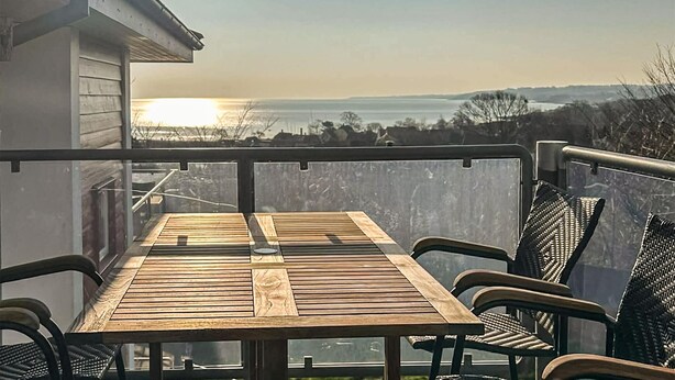 Una mesa de madera con sillas en un balcón con vista a un cuerpo de agua.