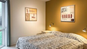 Un dormitorio con colcha estampada, mesita de noche, lámpara de pared y dos cuadros enmarcados.