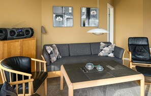 Un salon moderne avec un canapé gris, deux fauteuils en cuir noir, une table basse en bois et une radio posée sur un meuble.