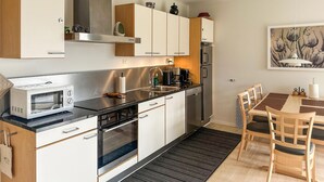 Cocina compacta con microondas, estufa y lavabo. Zona de comedor con mesa y sillas.