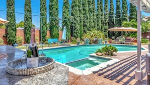 Une piscine agrémentée d’une pergola, de chaises longues et bordée d’arbres imposants.