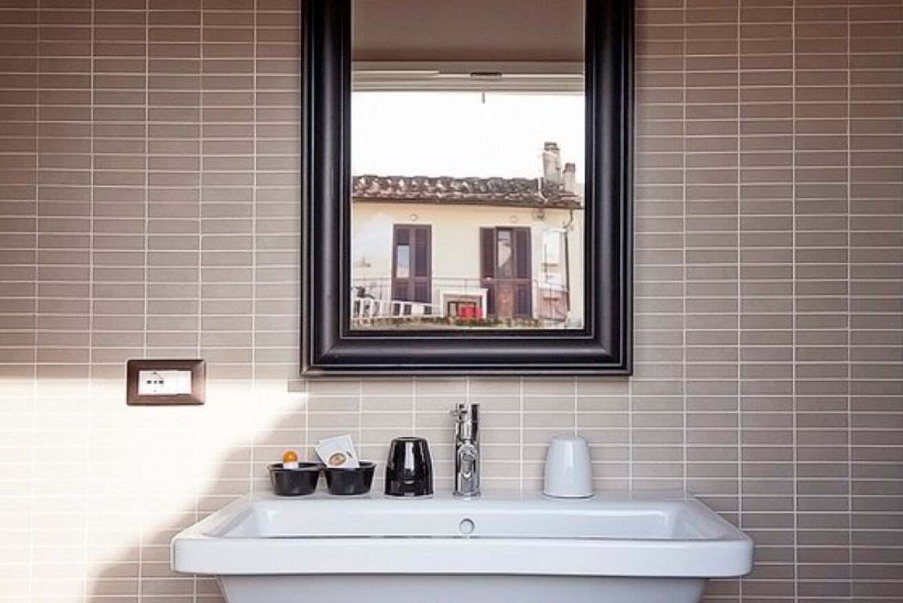 A bathroom with a white sink, a framed mirror, and a window with a view of buildings.