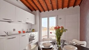 A modern kitchen with white cabinetry, a dining table set for two, and a view through the window. - Apartments Florence San Gallo Suite VII with balcony (Florence)