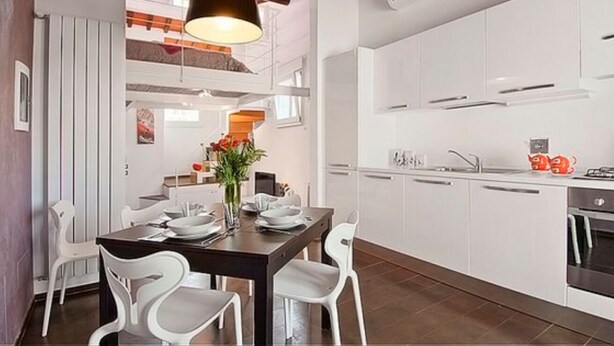 A modern kitchen with white cabinets, a dining table with chairs, and a hanging light fixture. - Apartments Florence San Gallo Suite VII with balcony (Florence)