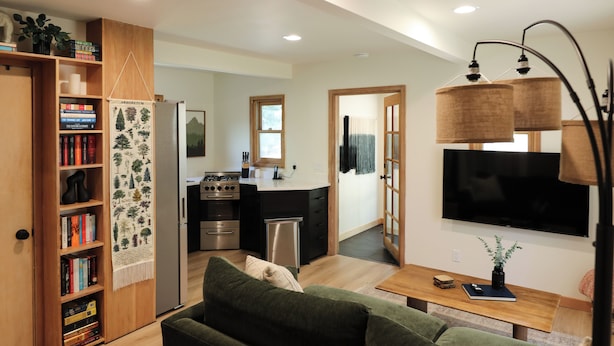 Una sala de estar moderna con un sofá verde, una estantería de madera y una cocina al fondo.