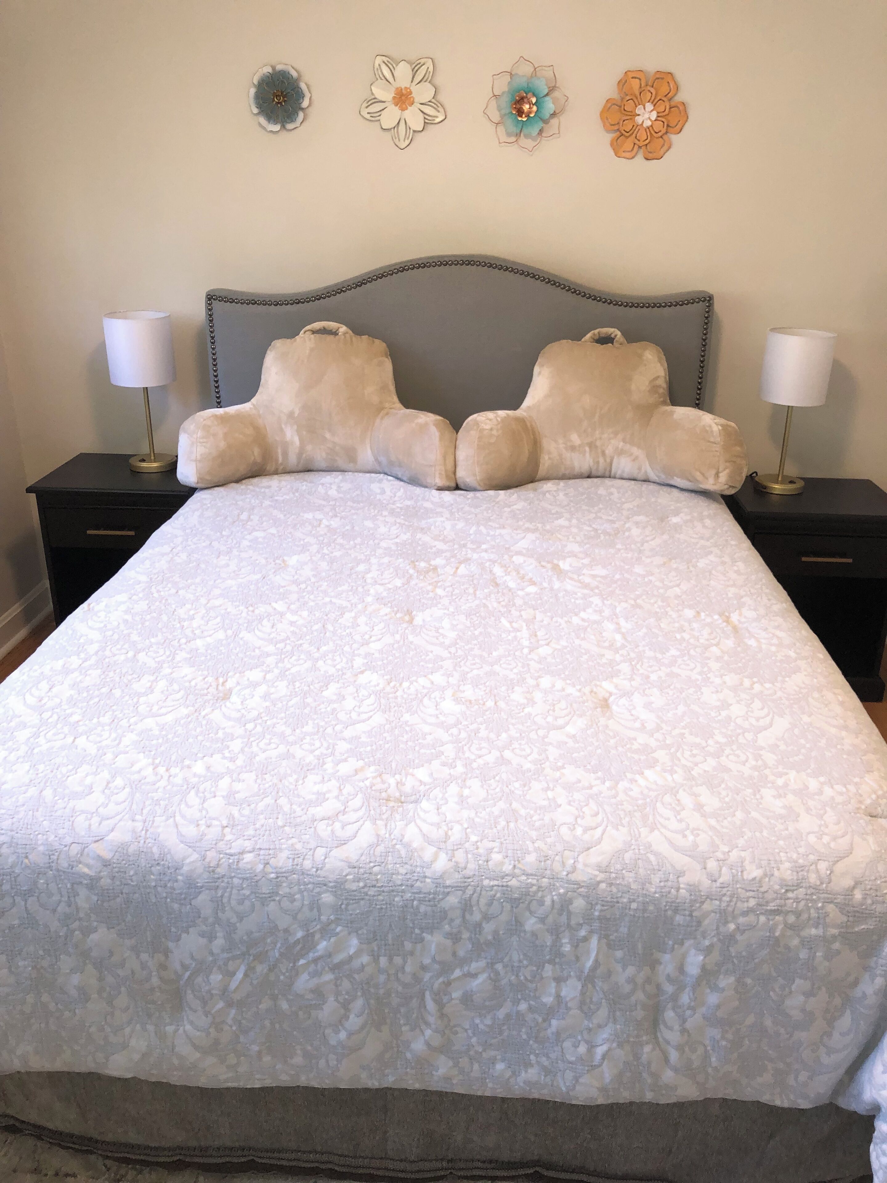 A neatly made bed with a patterned bedspread, two nightstands with lamps, and three wall-mounted flower decorations.