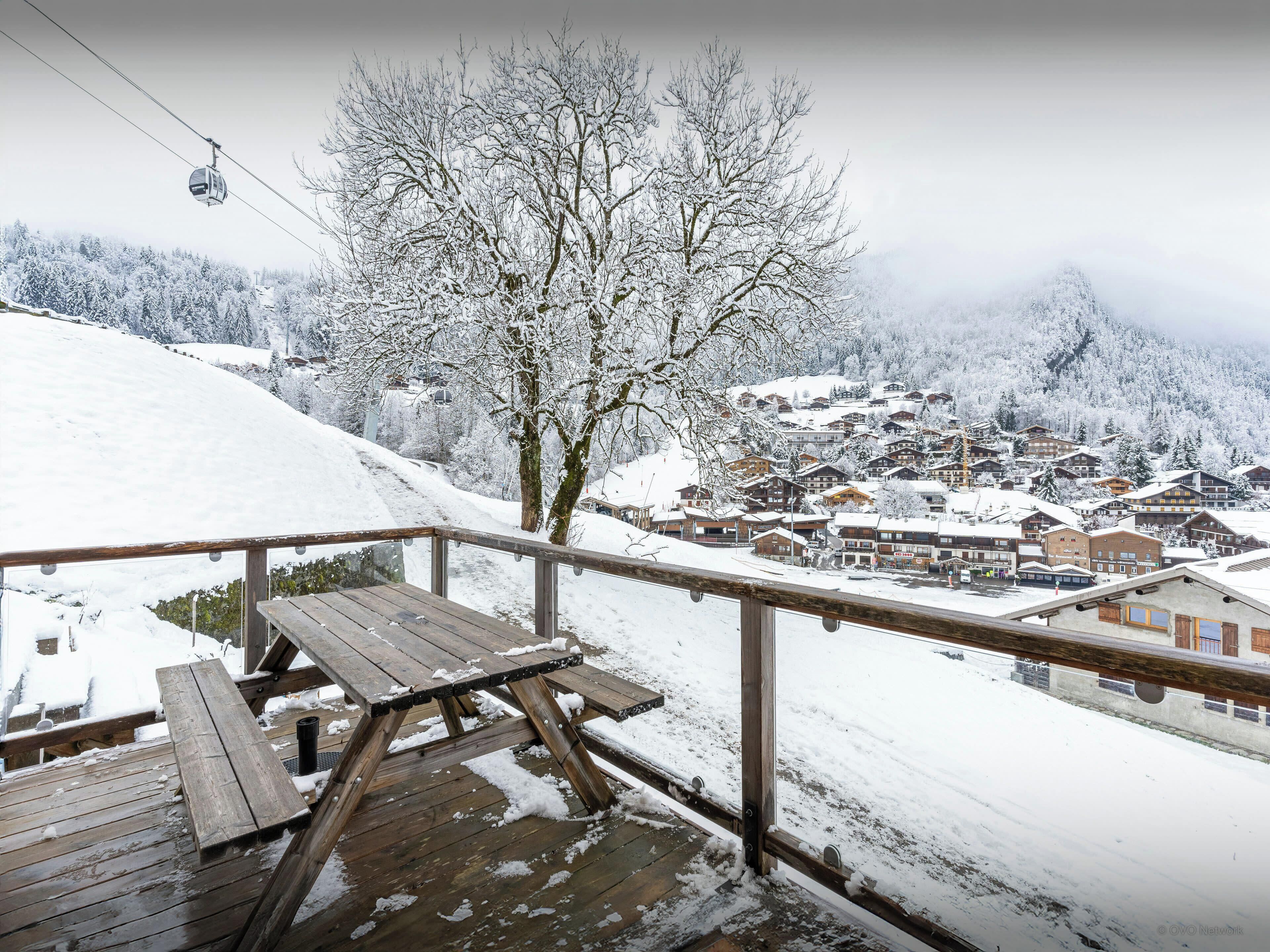A wooden deck with a picnic table and a snow-covered village in the background.