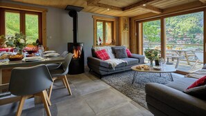A cozy living room with a fireplace, a dining area with a table set for a meal, and a balcony with a view of the surrounding landscape. - Le Petit Capricia - Aravis mountain stay for 8 - OVO Network (La Clusaz)