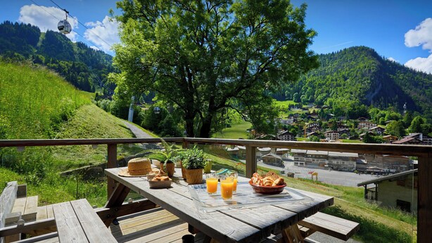 A wooden deck with a table set for breakfast, overlooking a scenic village and mountains. - Le Petit Capricia - Aravis mountain stay for 8 - OVO Network (La Clusaz)