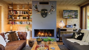 A cozy living room with a fireplace, leather sofas, a coffee table with snacks, and a bookshelf. - Le Grand Capricia - mountain stay with sauna - OVO Network (La Clusaz)