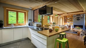 A modern kitchen with a central island, wooden beams on the ceiling, and a dining area with a fireplace. - Le Grand Capricia - mountain stay with sauna - OVO Network (La Clusaz)