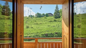 A wooden door leading to a balcony with a view of a green hillside and a distant building. - Le Grand Capricia - mountain stay with sauna - OVO Network (La Clusaz)
