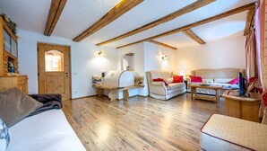 A cozy room with wooden beams, a sofa, a chair, a small table, and a wooden cabinet. - Apartments Smidl 110D (Ortisei)