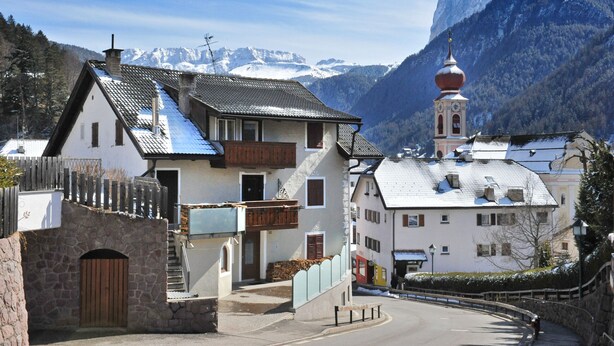 A traditional chalet with a stone entrance, a wooden fence, and a bell tower. - Apartments Smidl 110D (Ortisei)