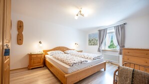 A bedroom with a wooden bed, bedside tables, a dresser, a window with curtains, and a radiator. - Apartments Smidl 110D (Ortisei)
