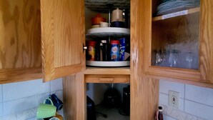 A kitchen with wooden cabinets, a white tiled floor, and various kitchen items including a kettle, coffee maker, and containers. - The Getaway (Placerville)