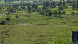 Un paysage rural avec des collines ondoyantes, une montagne en arrière-plan et une clôture en fil barbelé au premier plan.