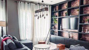 Un salon moderne avec des canapés gris, une table basse ronde et une bibliothèque dont les étagères sont décorées d’un motif imitant des briques.