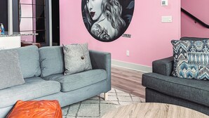 Un salon moderne avec un mur d’accent rose, un canapé gris, une table basse en bois et un pouf en cuir.