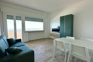 A room with a sofa, a table, a TV, and a view of the beach.