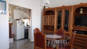A dining area with a round table and chairs, a kitchen with cabinets and appliances, and a television on a wooden cabinet. - SE118 - Senigallia, large three-room apartment with balcony (Senigallia)