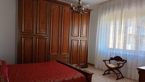 A bedroom with a bed, a wooden wardrobe, a chair, and a window with sheer curtains. - SE118 - Senigallia, large three-room apartment with balcony (Senigallia)