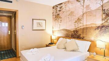 Una habitación de hotel con cama, mesita de noche, lámpara de pared, cuadro enmarcado y una puerta.
