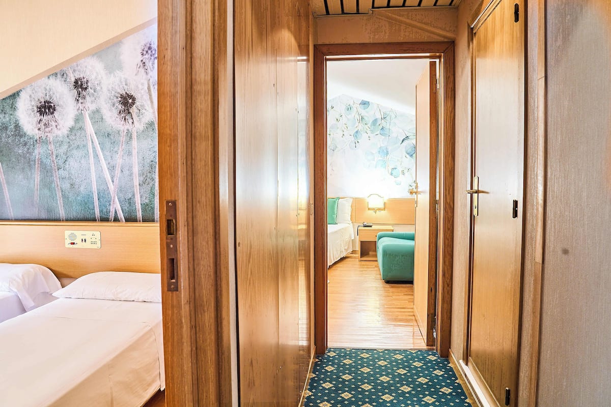 A hotel room with a bed, a bedside table, and a wall-mounted control panel.