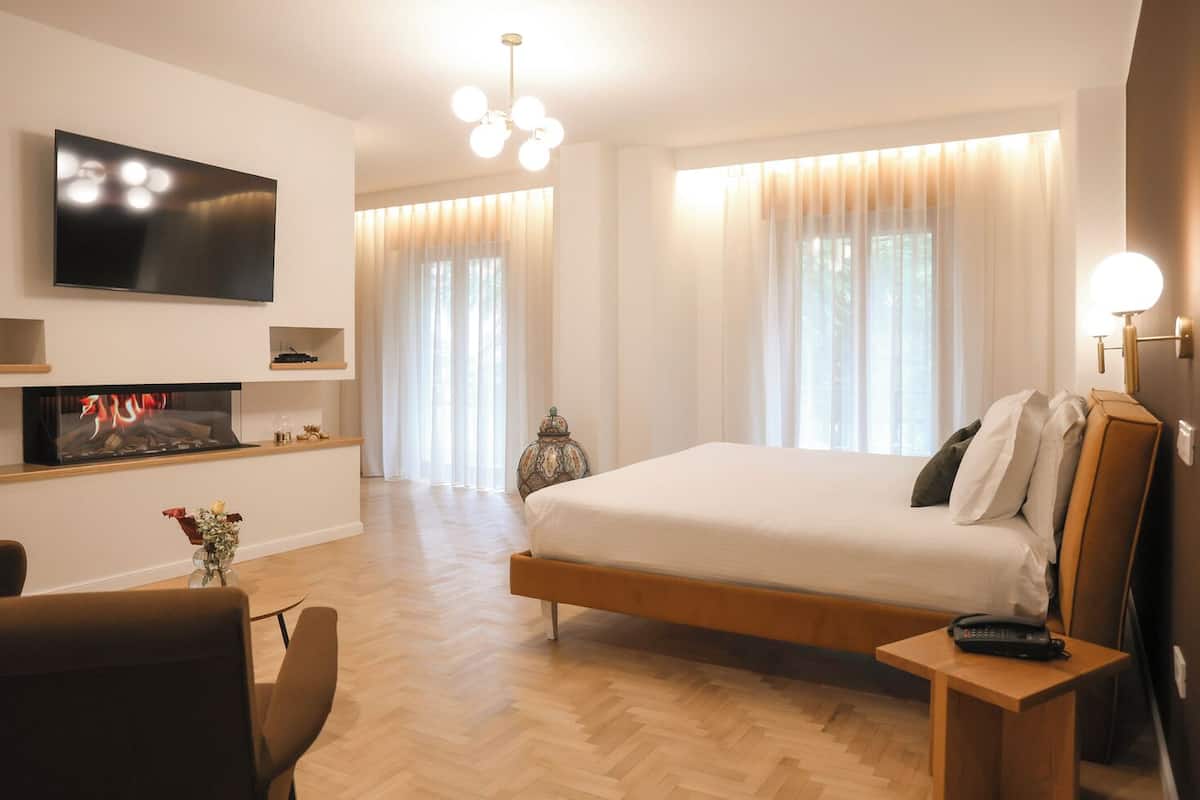 A modern hotel room with a large bed, a flat-screen TV mounted on the wall, a small table with a remote control, and a decorative vase with flowers.